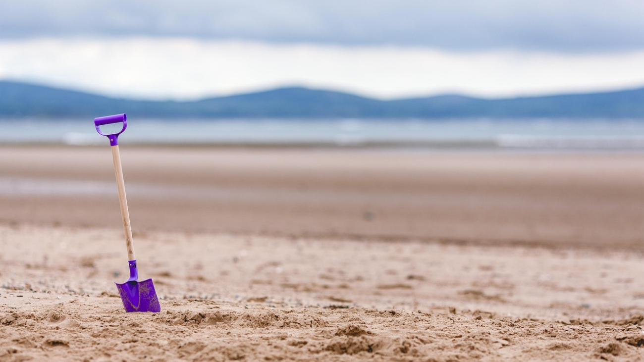 Bunte Schaufel steckt im Sand, dahinter Berge