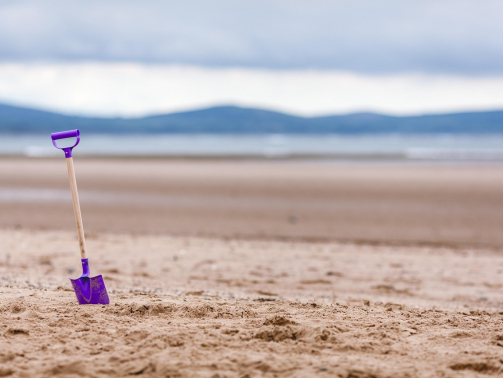 Bunte Schaufel steckt im Sand, dahinter Berge