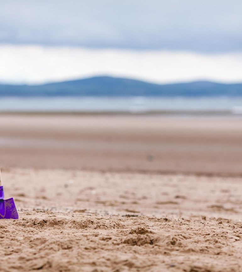 Bunte Schaufel steckt im Sand, dahinter Berge