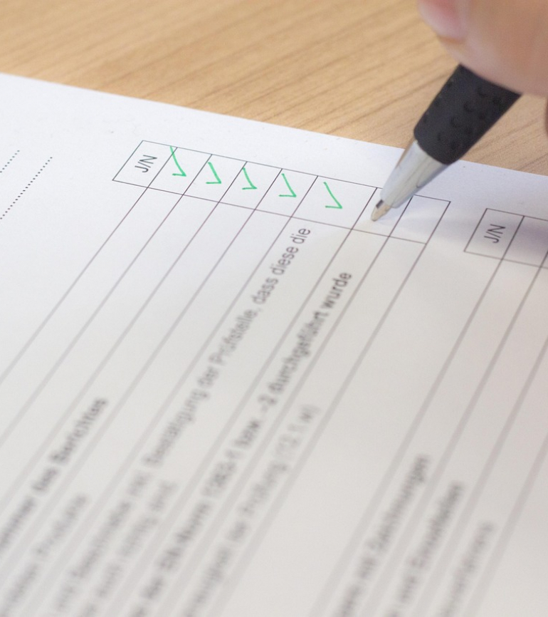 Hand mit einem Stift auf Blatt Papier und füllt eine Checkliste aus