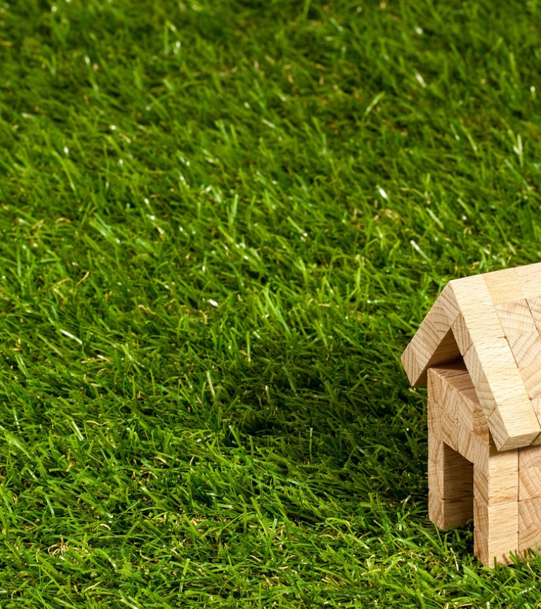 Miniaturhaus aus Holz auf grüner Wiese