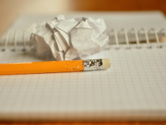 Bleistift mit Radiergummi liegt auf einem karierten Notizblock mit Spirale. Hinter dem Bleistift ein zusammengeknülltes Papier