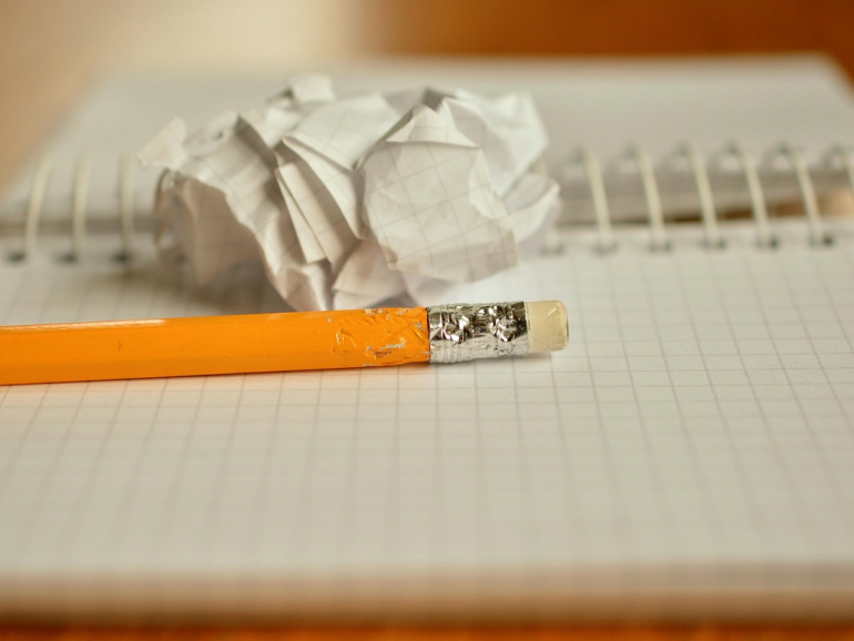 Bleistift mit Radiergummi liegt auf einem karierten Notizblock mit Spirale. Hinter dem Bleistift ein zusammengeknülltes Papier